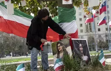 A woman places photographs of Mahsa Amini on a tree in front of the Palacio de la Moneda as Iranians living in Chile protest against violence against women in their country, during the International Day for the Elimination of Violence against Women in Santiago, on November 25. [Martin Bernetti/AFP]