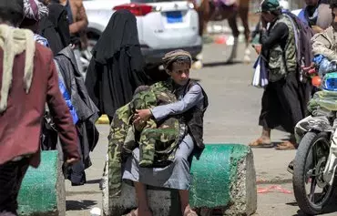 یک دستفروش جوان در روز ۴ فروردین ۱۴۰۱ روی یک بلوک سیمانی نشسته است. او ژاکت‌هایی با طرح موسوم به چریکی در دست دارد و آنها را به عابران در خیابانی در صنعا، پایتخت یمن، می‌فروشد. [محمد حویس/ خبرگزاری فرانسه]
