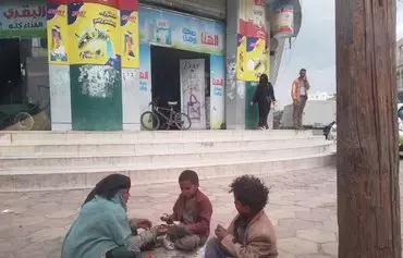 A mother and her children eat on the sidewalk outside a shopping center in Sanaa in this undated photo. The war continues to cast a shadow on all aspects of life in Yemen. [Yazan Abdul Aziz/Al-Fassel]
