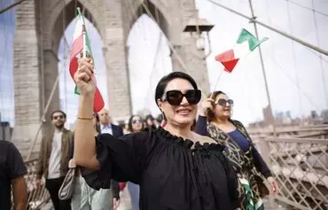 Women waves Iranian flags on the Brooklyn Bridge during a global protest in solidarity with Iranian women in New York on September 16, on the first anniversary of the death of Iranian Kurd Mahsa Amini in custody. [Kena Betancur/AFP]