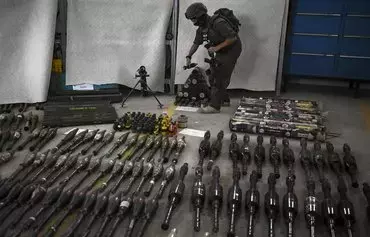 یک سرباز اسرائیلی در روز ۴ آبان در کنار مجموعه‌ای از تسلیحات ایستاده است. این سلاح‌ها از مناطقی که حماس در حملهٔ تروریستی خود در روز ۱۵ مهر به جنوب اسرائیل هدف قرار داده بود، به‌دست آمده است. [آریس مسینیس/ خبرگزاری فرانسه]
