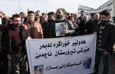 Protesters hold pictures of children's bodies and a banner reading 'Erbil remains resilient, and it does not kneel down to terrorist attacks,' during a demonstration on January 16 outside the United Nations (UN) office, a day after several areas in the city were hit by an IRGC missile attack. [Safin Hamid/AFP]
