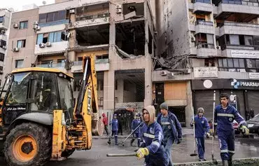 روز ۱۳ دی‌ماه روبه‌روی ساختمانی در حومهٔ جنوبی بیروت، کارگران شهرداری در حال تمیز کردن خیابان هستند؛ صالح العاروری، معاون سیاسی حماس، یک روز پیش‌تر در همین محل طی یک حملهٔ پهپادی کشته شده بود. [انور عمرو/خبرگزاری فرانسه]