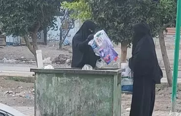 زنان در محلهٔ بیت بوس صنعا در یک سطل زباله به‌دنبال پس‌مانده‌های غذا می‌گردند. [یزان عبدالعزیز/الفاصل]