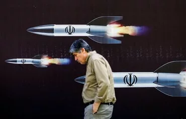 A man walks past a banner depicting missiles along a street in Tehran on April 19. [AFP]