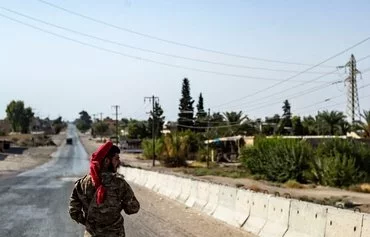 A member of the Syrian Democratic Forces (SDF) stands guard amid a curfew in al-Busayrah, Deir Ezzor, last September 4 following clashes between the SDF and tribal fighters. [Delil Souleiman/AFP]