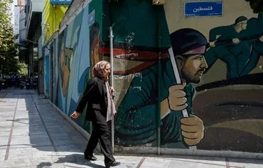 A woman walks past a mural depicting members of the IRGC, in Tehran on August 8. [AFP]