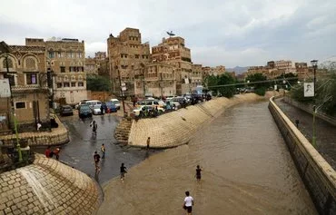 People wade in the water on a flooded street following heavy rainfall in the old city of Sanaa on August 1, 2022. [Mohammed Huwais/AFP]