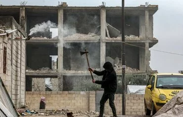 A man chops firewood near a building damaged in the earthquake of February 2023 in the Aleppo town of Jindayris on February 5, 2024. Newly sanctioned IRGC-QF Unit 700 is accused of smuggling weapons into Syria under the pretext of providing earthquake aid. [Bakr Alkasem/AFP]