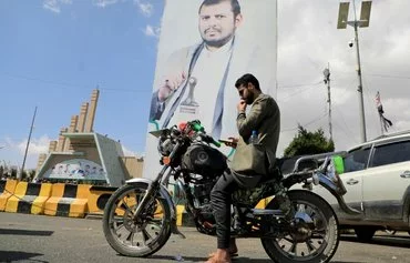 A man checks his phone near a portrait of Houthi leader Abdul Malik al-Houthi, on January 18 in Sanaa. [Mohammed Huwais/AFP]